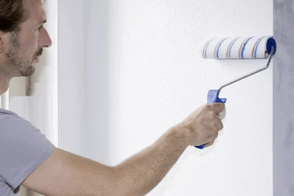 Person streicht Wand mit Farbrolle
